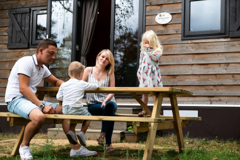 Een gezin zit aan een picknicktafel voor een stacaravan bij Holiday Park Ardinam 1 in België.