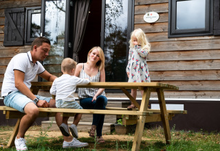 Eine Familie sitzt an einem Picknicktisch vor einem Mobilheim im Holiday Park Ardinam 1 in Belgien.