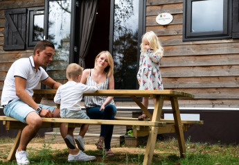 Una famiglia seduta a un tavolo da picnic davanti a una casa mobile a Holiday Park Ardinam 1 in Belgio.