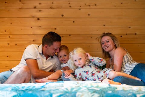 Gezin relaxt samen in een stacaravan bij Holiday Park Ardinam 1 in België, met houten wand op de achtergrond.