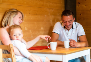 Gezin geniet samen van koffie aan tafel in het mobil home Holiday Park Ardinam 1 in België.