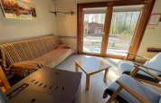 Innenaufnahme des Chalets LIJSTERNEST in Belgien mit Karo-Sofa, Holztisch und Blick nach draußen.