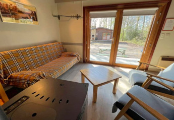 Innenaufnahme des Chalets LIJSTERNEST in Belgien mit Karo-Sofa, Holztisch und Blick nach draußen.