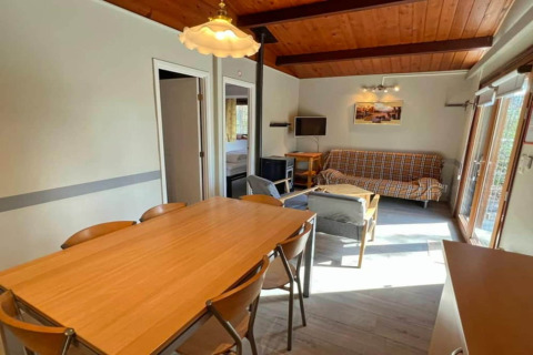 Salon et salle à manger chaleureux au chalet LIJSTERNEST en Belgique, plafond bois, canapé et grande table.