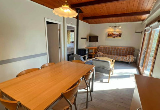 Salon et salle à manger chaleureux au chalet LIJSTERNEST en Belgique, plafond bois, canapé et grande table.