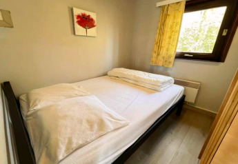 Kleines Schlafzimmer mit Doppelbett, weißer Bettwäsche, Fenster und rotem Blumenbild an der Wand.