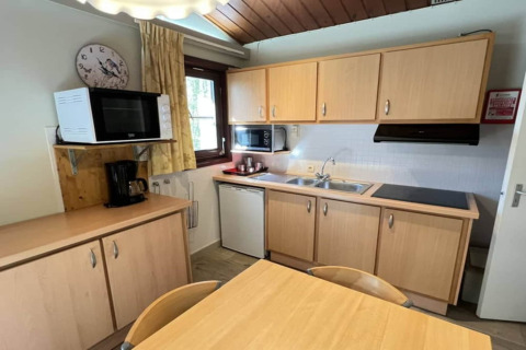 Cuisine du chalet LIJSTERNEST en Belgique avec meubles en bois, micro-ondes, cafetière et table à manger.