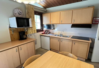Cuisine du chalet LIJSTERNEST en Belgique avec meubles en bois, micro-ondes, cafetière et table à manger.
