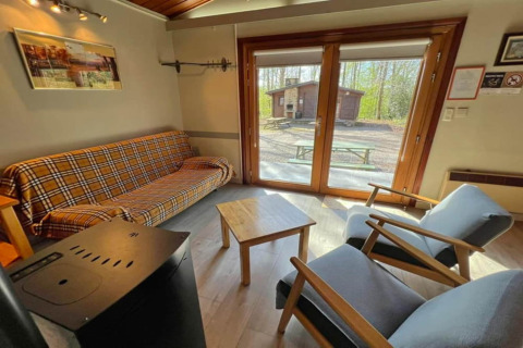 Salon du chalet LIJSTERNEST en Belgique, canapé à carreaux et vue sur l'extérieur boisé.
