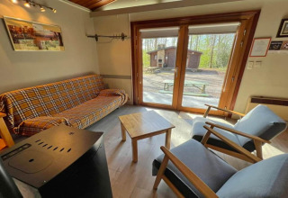 Salon du chalet LIJSTERNEST en Belgique, canapé à carreaux et vue sur l'extérieur boisé.