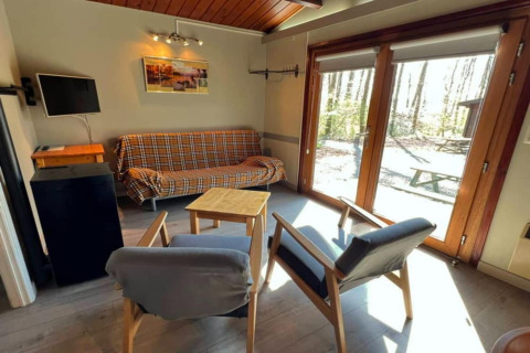 Salon lumineux du chalet LIJSTERNEST en Belgique avec canapé à carreaux et vue sur la forêt.