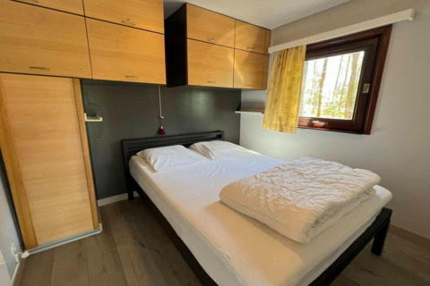 Chambre au chalet LIJSTERNEST en Belgique avec lit double, placards en bois clair et fenêtre lumineuse.