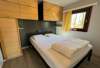 Chambre au chalet LIJSTERNEST en Belgique avec lit double, placards en bois clair et fenêtre lumineuse.