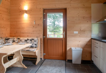 Interior of Rogery 64 chalet in Belgium featuring wood walls, dining table, and door with outside view.