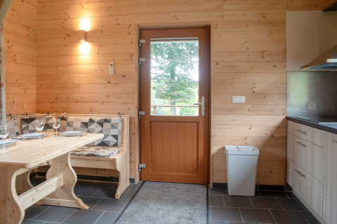 Interieur van chalet Rogery 64 in België met houten muren, eettafel en deur met uitzicht naar buiten.