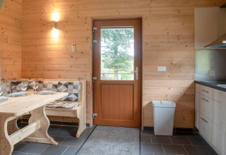 Interieur van chalet Rogery 64 in België met houten muren, eettafel en deur met uitzicht naar buiten.