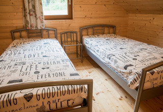 Twee eenpersoonsbedden met tekstdekbedovertrek in een houten kamer van chalet Rogery 64 in België.