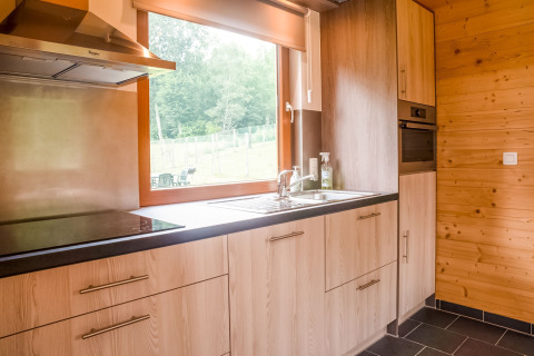 Moderne keuken in chalet Rogery 64 in België, met houten kasten, groot raam en zwart werkblad.