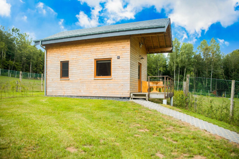 Knus houten chalet Rogery 64 in België, omringd door groene velden en bos, onder een stralend blauwe lucht.