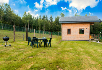 Chalet Rogery 64 in Belgium with wooden cabin, lawn, outdoor dining set, BBQ grill and forest background.