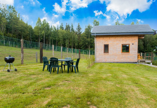 Chalet Rogery 64 in België met houten huisje, tuinset, barbecue en grasveld naast een bosrijke omgeving.
