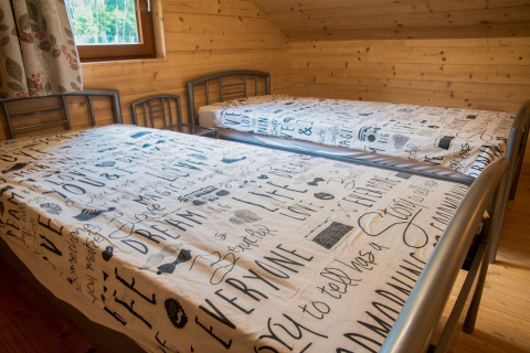 Twee eenpersoonsbedden met beddengoed in houten kamer van chalet Rogery 64, België, raamzicht aanwezig.