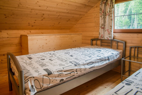 Slaapkamer met houten wanden, eenpersoonsbedden en raam in chalet Rogery 64 in België overdag.