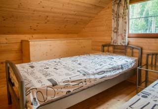 Slaapkamer met houten wanden, eenpersoonsbedden en raam in chalet Rogery 64 in België overdag.
