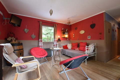 Hyggelig stue i chalet Flons et Roulotte i Belgien med røde vægge, stole, sofa og dekorative detaljer.