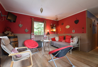 Hyggelig stue i chalet Flons et Roulotte i Belgien med røde vægge, stole, sofa og dekorative detaljer.