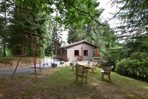 Hyggeligt chalet Flons et Roulotte i skoven, med gyngestativ, stole og terrasse, omgivet af træer.