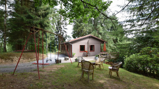 Chalet Flons et Roulotte in the woods, with swings, outdoor chairs, and a deck, surrounded by trees.