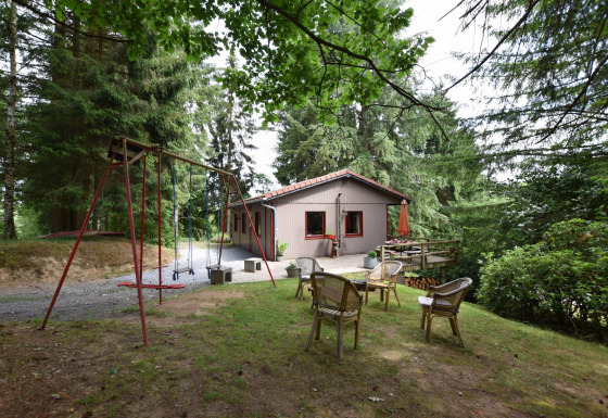 Hyggeligt chalet Flons et Roulotte i skoven, med gyngestativ, stole og terrasse, omgivet af træer.