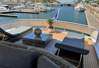 Luxury seating area on Yacht Aquamarina with loungers and stylish decor, docked in a vibrant marina.