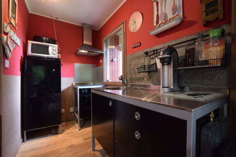 Moderne køkken i chalet Flons et Roulotte i Belgien med sort køleskab, mikrobølgeovn og rød væg.