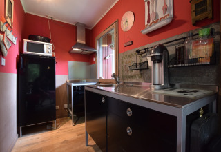 Moderne køkken i chalet Flons et Roulotte i Belgien med sort køleskab, mikrobølgeovn og rød væg.
