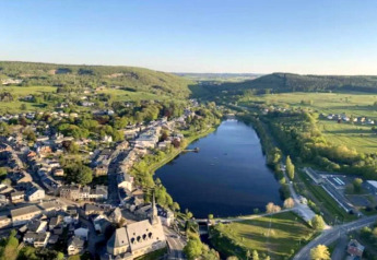 Aerial view of a lake, village and green fields captured from the Rogery 64 chalet in Belgium.
