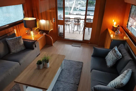 Modern living room on houseboat Yacht Aquamarina featuring cozy sofas, water views, and outdoor seating area.
