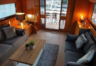 Modern living room on houseboat Yacht Aquamarina featuring cozy sofas, water views, and outdoor seating area.