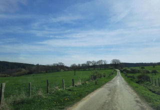 Landschapsfoto vanaf chalet Rogery 64 in België, met een weg, groene velden en een blauwe lucht.