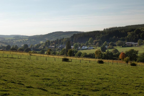 Uitzicht vanaf chalet 'Rogery 64' in België op glooiende groene velden, dorpshuizen en bossen.