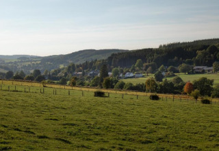 Uitzicht vanaf chalet 'Rogery 64' in België op glooiende groene velden, dorpshuizen en bossen.