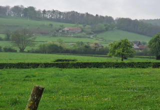 Uitzicht vanuit chalet Rogery 64 in België over groene weiden, bomen en huizen in een heuvelachtig landschap.