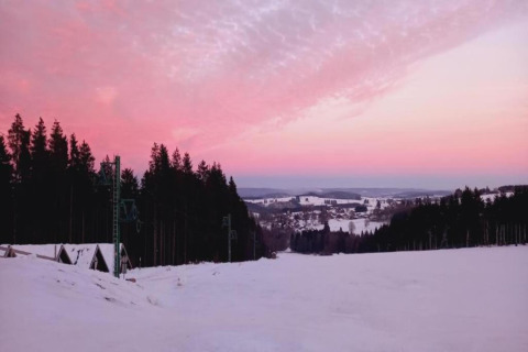 Zonsondergang boven een besneeuwd landschap met bossen bij chalet Rogery 64 in België, roze lucht.