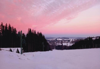 Zonsondergang boven een besneeuwd landschap met bossen bij chalet Rogery 64 in België, roze lucht.