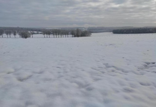 Met sneeuw bedekt landschap en velden met bomen, gezien vanaf chalet Rogery 64 in België onder een bewolkte lucht.