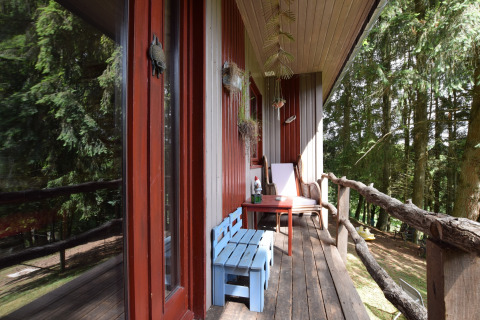 Hyggelig balkon ved Flons et Roulotte chalet i Belgien, med blå bænk, stol og udsigt til skov.