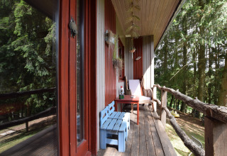 Hyggelig balkon ved Flons et Roulotte chalet i Belgien, med blå bænk, stol og udsigt til skov.