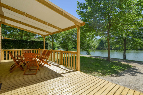 Overdekte houten veranda met tuinmeubilair, uitzicht op meer en bomen bij Cottage «6p» in Frankrijk.