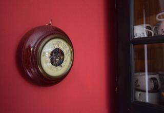 Et barometer med træramme hænger på en rød væg i et chalet ved navn 'Flons et Roulotte' i Belgien.